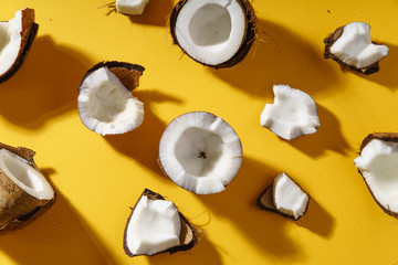 Cracked coconut and coconut pieces on yellow background. Overhead view