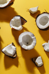 Cracked coconut and coconut pieces on yellow background. Overhead view