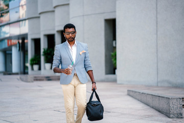 A young and handsome Indian Asian man walks down a street in Asia while drinking a coffee and...