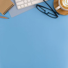 Flat lay, top view office table desk. Workspace with blank note book, keyboard, office supplies and coffee cup on light blue background.