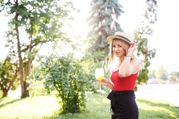 Young pretty blonde spends time in the park with a glass of cool cocktail in her hands