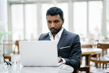 Portrait of an Indian man in a 3-piece suit working on his notebook computer during the day.