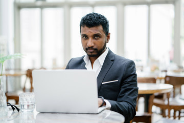 Portrait of an Indian man in a 3-piece suit working on his notebook computer during the day.