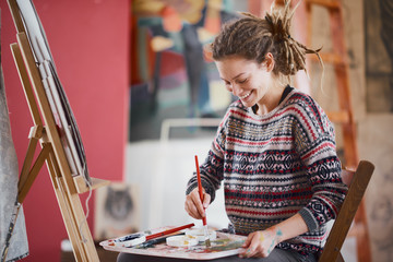 Naklejka premium Artistic girl sitting in studio and paint on easel.