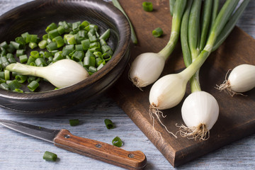 Young fresh green onion on a wooden cutting board on an old table. 