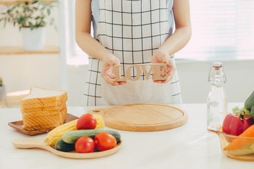 A woman holding wooden letter LOVE while cooking in the kitchen.