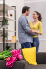 bouquet of tulips lying on couch with beautiful adult couple embracing blurred on background