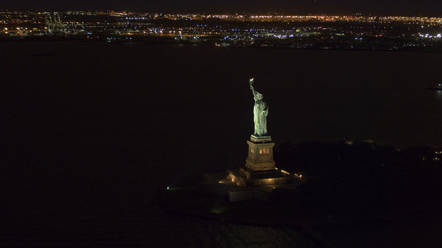 AERIAL, CLOSEUP: Iconic Statue od Liberty lit up at night shining in the dark