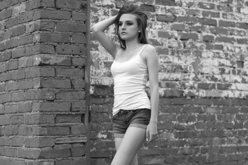 girl in a T-shirt and shorts stands by the brick wall