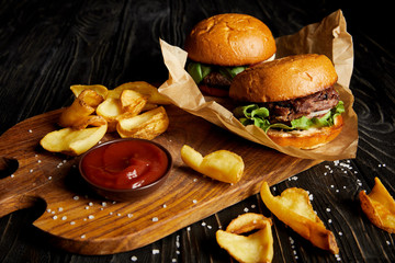 Tempting fast food diner with burgers and potatoes with sauce on cutting board - obrazy, fototapety, plakaty