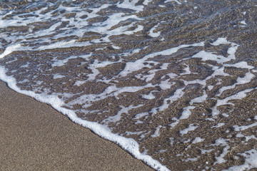 Texture of foamy wave and sand on the beach, background