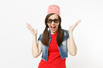 Obraz na płótnie Canvas Portrait of young overjoyed attractive woman in 3d glasses and casual clothes with bucket for popcorn on head watching movie film and spreading hands isolated on white background. Emotions in cinema.