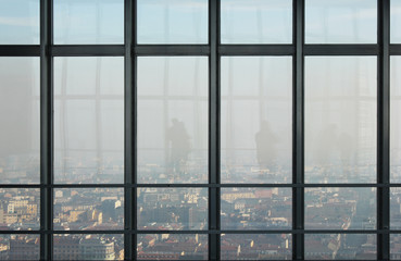 window on top of a skyscraper with a view of Milan and people silhouette reflection.