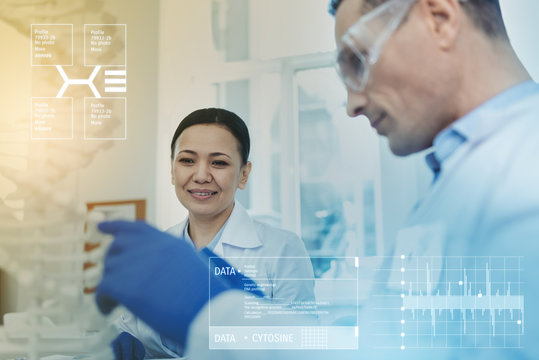 Studying chains. Clever professional biologist smiling while sitting in a lab next to her experienced colleague