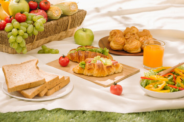 Picnic wicker basket with food, bread, fruit and orange juice on a red and white checked cloth in the field with green nature background. Picnic concept.