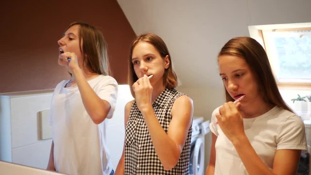 Brush teeth in front of the bathroom mirror three girls teenager sisters before going to bed