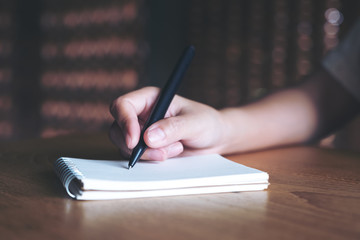 Closeup image of a woman's hand writing down on a white blank notebook on wooden table