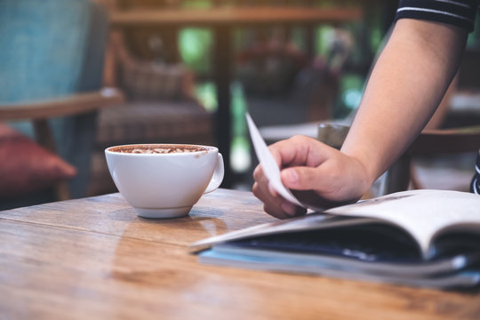 Closeup image of a woman reading a magazine with coffee cup on table in cafe