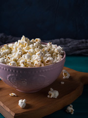 Popcorn in pink bowl on wooden board on dark background