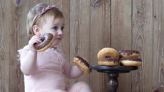 food for children, infant eating sweet chocolate donuts on background of wooden wall