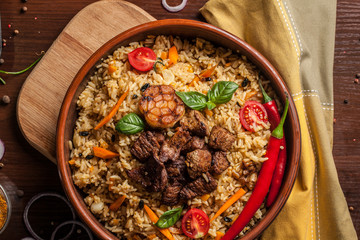 Uzbek restaurant concept, Uzbek food feast. Uzbek pilaf made from beef, lamb, chicken, in large earthenware, plate, next to vegetables. Copy space