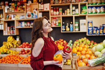 Girl in red holding different vegetables on fruits store.