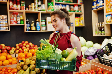 Girl in red holding different vegetables on fruits store.