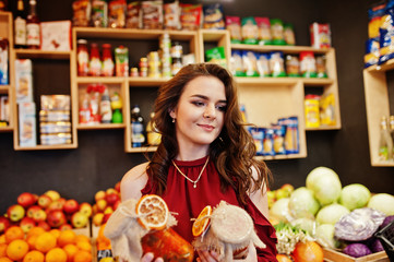Girl in red holding jam in a jar on fruits store.