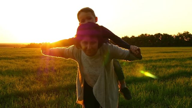 Mom and child, happy to show their hands flying an airplane in nature. Beautiful family mom and boy. Mom keeps the baby on her back