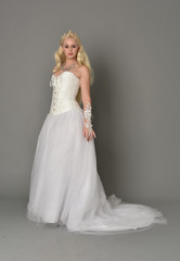Fototapeta premium full length portrait of blonde girl wearing white corset gown. standing pose on grey studio background.