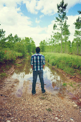 Fototapeta na wymiar Hombre joven junto a un camino inundado de agua que se ha hecho un río