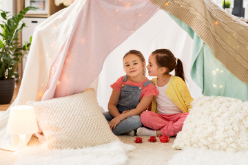 childhood and hygge concept - happy little girls playing tea party with toy crockery in kids tent...