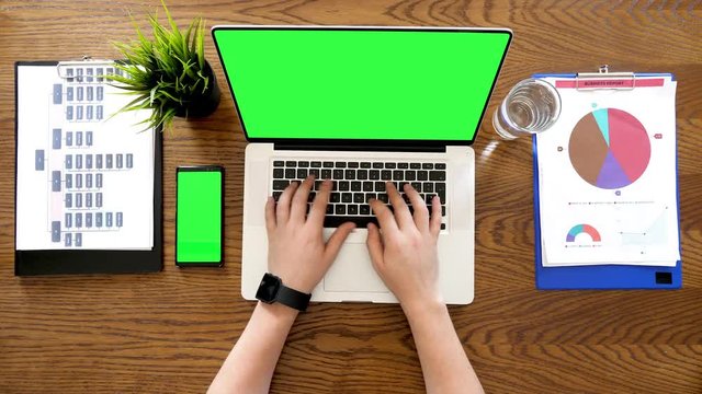 Male hands typing on laptop with a chroma green screen next to a phone with chroma on it also. Top view footage on a business desk