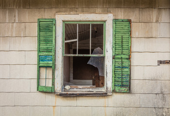 Obraz premium Broken window with green shutters on old rustic abandoned barn surrounded by bright fall foliage