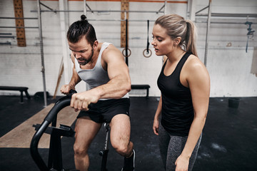 Fit man riding a stationary bike with his gym partner