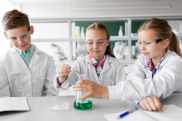Obraz premium education, science, chemistry and children concept - kids or students with test tube making experiment at school laboratory