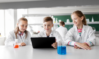 education, science and technology concept - kids with tablet pc computer studying chemistry at school laboratory