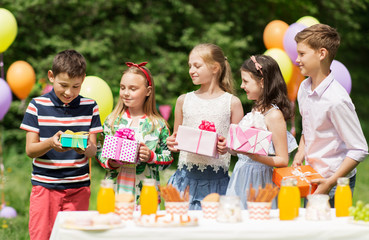 holidays, childhood and celebration concept - happy kids with gifts on birthday party at summer garden