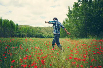 Hombre joven disfrutando de un día de primavera en un campo de trigo y amapolas 