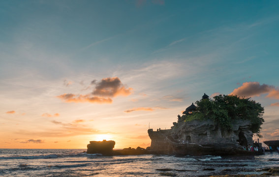 Silhueta de templo hindu Tanah Lot na praia, em Bali (Indonésia), durante pôr do sol com céu colorido de azul e laranja