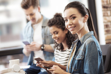 Social networking. Joyful nice woman smiling while typing a message on her smartphone