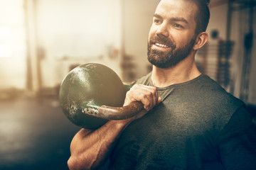 Smiling young man holding a dumbell at the gym