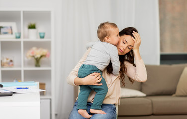 motherhood, multi-tasking and family concept - tired working at home mother with baby having...