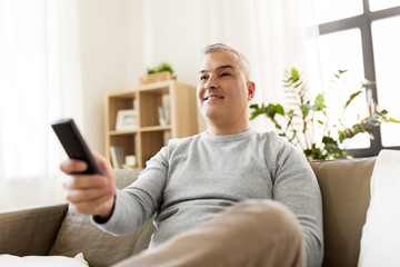 people, television and entertainment concept - smiling man with remote control watching tv at home