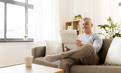 leisure, information, people and mass media concept - happy smiling man reading newspaper at home