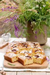 Pieces of fruit pie with pieces of plums and peach and a bouquet of flowers on a wooden table. Rustic style.