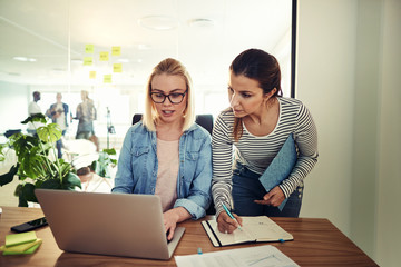 Two businesswomen working online and writing notes in an office
