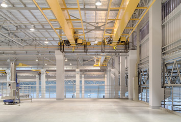 Concrete floor inside factory or warehouse building with empty space for industry background. Overhead crane or bridge crane include hoist lifting for transportation, manufacturing, and production.