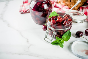 Homemade preserved cherry and mint jam, with fresh cherries on white marble background copy space