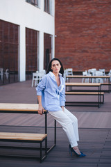 Fototapeta premium A beautiful woman in a shirt and pants sits on a balcony of a building.
